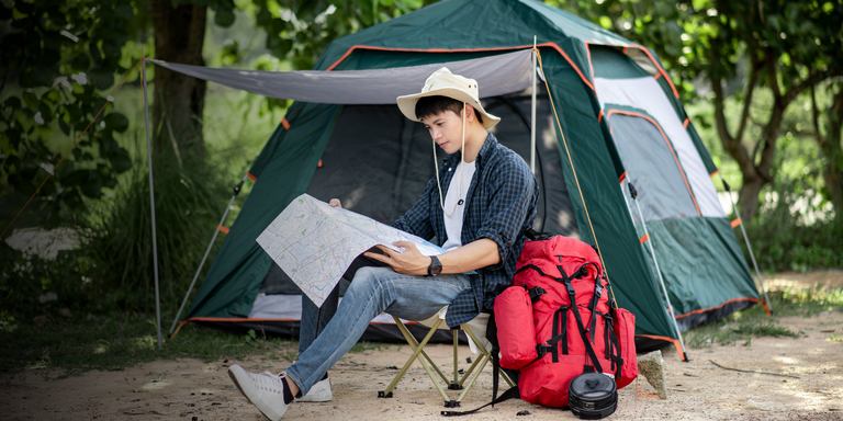 Person sitting in front of a tent with a map, surrounded by nature

